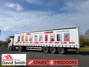 Side view of a white lorry covered in DSSI imagery and branding on a road on a sunny day.